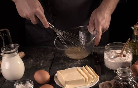 Hands of pastry chef beat eggs in glass bowl, isolated on black backgroundの写真素材