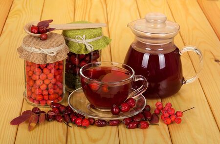 Banks with dry fruits of mountain ash and wild rose, pitcher and Cup with a vitamin drink on beige wooden tableの写真素材