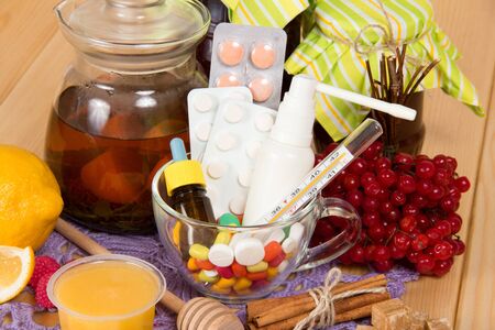 Hot tea with honey and lemon, cup with pills, drops and spray on wooden surfaceの写真素材