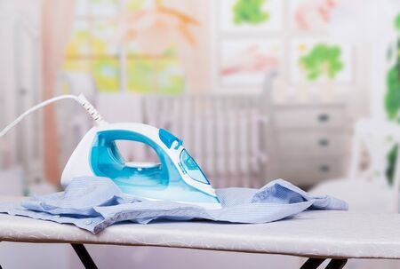 Functional modern iron on the Ironing Board and children's shirt on light backgroundの写真素材