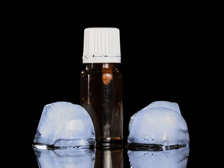 Aromatic liquid for inhalation vapor electronic cigarettes, next to two ice cubes isolated on black backgroundの写真素材