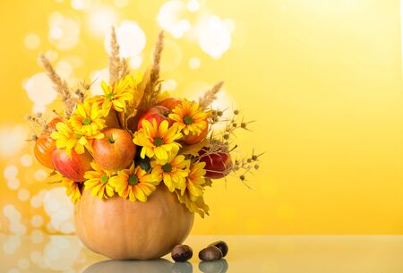 Original bouquet from flowers and fruits in pumpkin vase, next to chestnuts on light yellow backgroundの写真素材