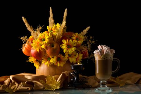 Cup of cappuccino with marshmallows, autumn bouquet and candle isolated on black backgroundの写真素材