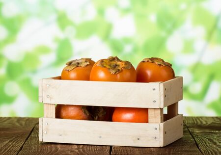 Wooden box with ripe sweet persimmons on dark wooden tableの写真素材