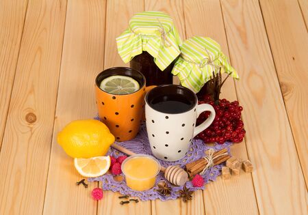 Jars with jam, cup of tea with lemon, honey and spices on wooden surfaceの写真素材