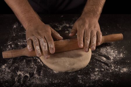 The baker's hands roll out the dough sheet, isolated on black backgroundの写真素材