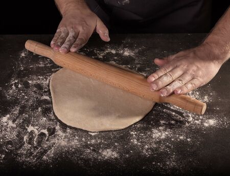 Baker rolls out the layer of dough with rolling pin, isolated on black backgroundの写真素材