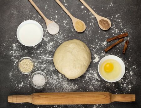 Ready-made dough lump, rolling pin, spoons with spices, against gray surfaceの写真素材