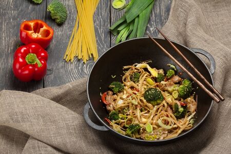 Traditional Asian dish, noodles with meat and vegetables in wok pan, chopsticks on burlapの写真素材