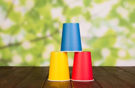 Three multi-colored plastic cups stand on each other, on brown wooden tableの写真素材