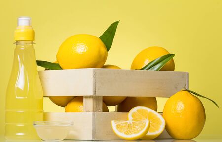 Wooden crate of lemons and pieces of fruit, juice in bottle, on bright yellow backgroundの写真素材