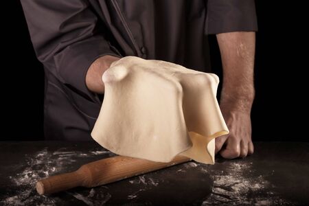 The rolled out layer of dough and rolling pin in the hands of Baker isolated on black backgroundの写真素材