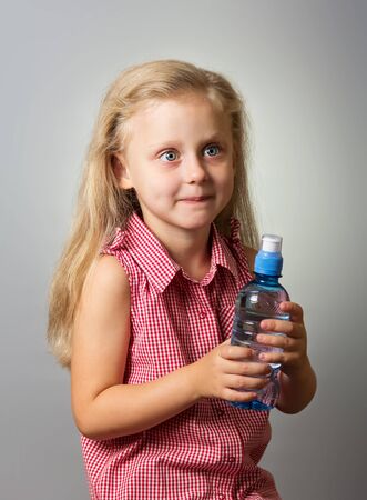 Adorable little girl with long hair holding a bottle of water on gray backgroundの写真素材