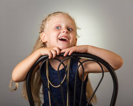 Smiling girl with long hair in dress with beads sitting on chair, on grey backgroundの写真素材