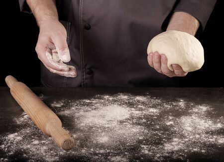Flour and rolling pin on work surface, clod of dough in Baker's hands, isolated on black backgroundの写真素材