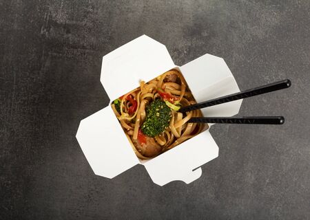 Noodles with meat and vegetables in wok box, on grey surface, top viewの写真素材