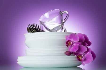 Stack of clean plates, cutlery and cups are top, near Orchid flower on lilac backgroundの写真素材