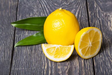 Slices of citrus and a whole lemon with leaves on dark wooden surfaceの写真素材