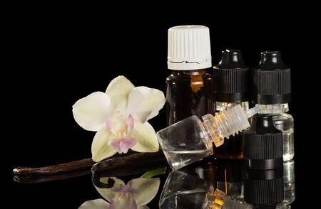 Bottles of aromatic liquid for vaping, vanilla pods and Orchid flower isolated on black backgroundの写真素材