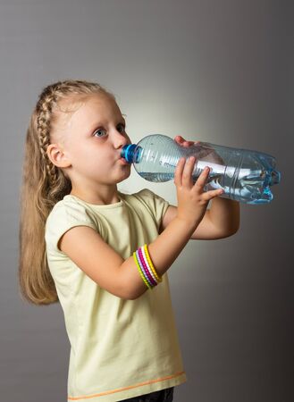Small girl with luxurious long hair drinks water from bottle, on grey backgroundの写真素材