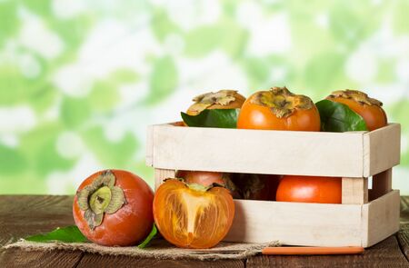 Wooden box with persimmon, near on burlap whole fruit, half and knife on wooden tableの写真素材