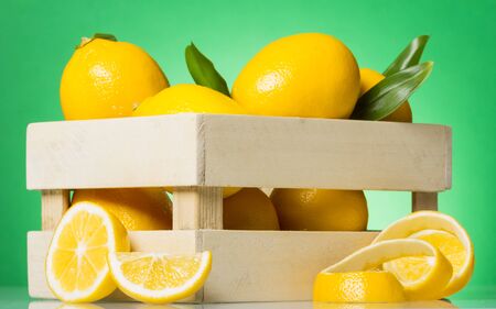 Wooden box with lemons, near slices and rind of citrus fruits on green backgroundの写真素材