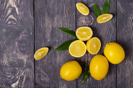 Bright yellow lemons with leaves and cut into pieces scattered on dark wooden surfaceの写真素材
