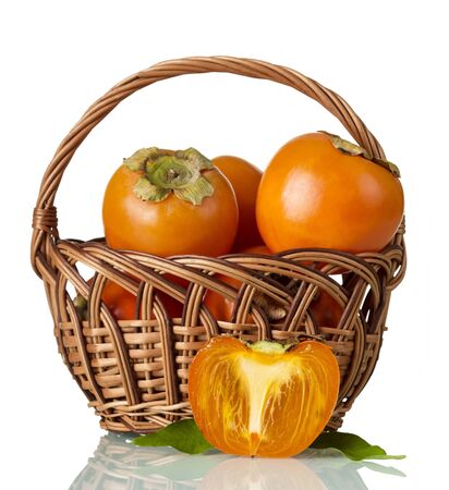 Persimmon in wicker basket, near half of fruit isolated on white backgroundの写真素材