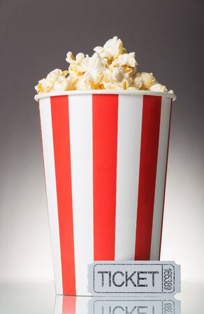 Red and white big cup of popcorn with movie tickets on a gray backgroundの写真素材