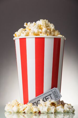 Box of popcorn, movie ticket and popcorn spilled on a gray backgroundの写真素材