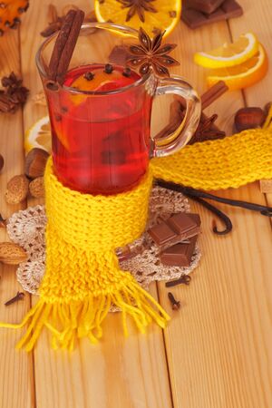 Mulled wine with orange, cloves, anise and cinnamon, nuts, chocolate chips, a yellow scarf on a background of light wood.の写真素材