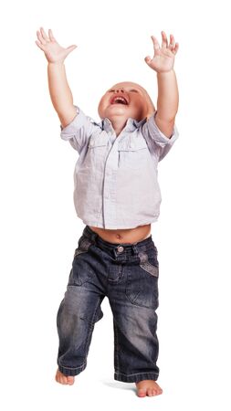 Merry little boy in a bright shirt with stripes and jeans with his hands raised up isolated on white background.の写真素材