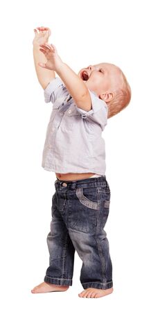 Happy little boy in a bright shirt with stripes and jeans with his hands raised up isolated on white background.の写真素材