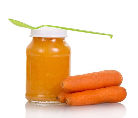 Jar of carrot puree with a spoon isolated on white background.の写真素材