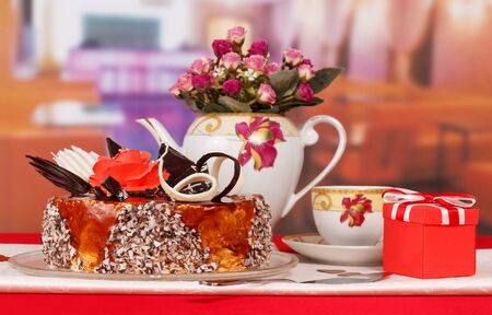 Chocolate cake, cup of tea, a gift and a bouquet of roses on a background of the kitchen.の写真素材