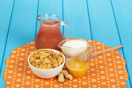 Healthy breakfast. A bowl of cornflakes, a jug of juice, yogurt, honey and peanuts on the wooden background painted in blue.の写真素材