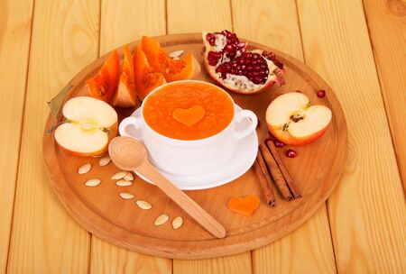 A bowl of pumpkin pureeand garnet, apples, seeds and spoon on a background of light wood.の写真素材