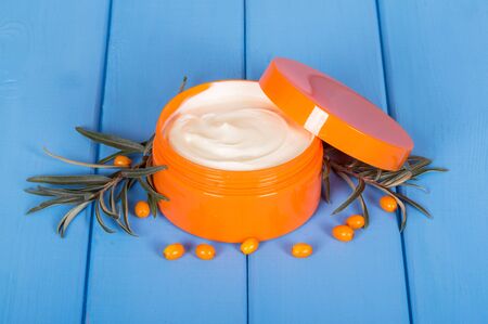 Bunch of sea buckthorn and jar with cream on a background of blue painted wood.の写真素材