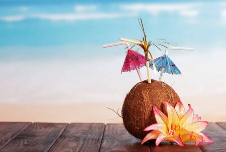 Coconut with straw umbrellas and flower on a brown table against the sea.の写真素材