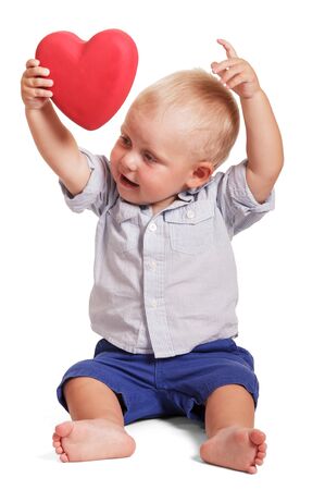 Little boy is sitting, his hands raised up and hold red heart isolated on white background.の写真素材