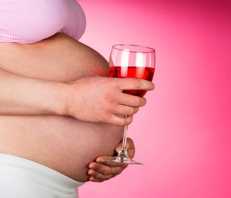 Pregnant woman with a glass of red wine in hand on a pink background.の写真素材