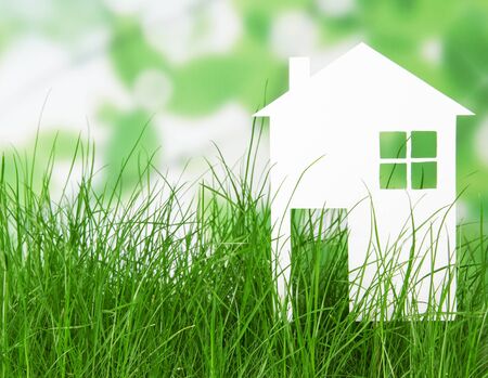 Small house from a white paper in the grass on abstract green background. Concept.の写真素材