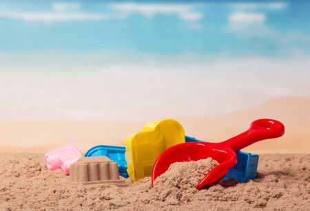 Bright plastic toys and a sand castle in the sand against the sea.の写真素材