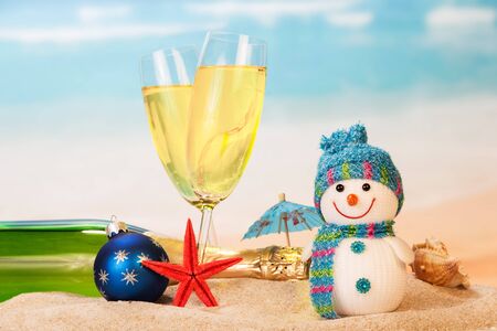 Bottle and two glasses of champagne, snowman, Christmas ball, starfish, shell in the sand against the sea.の写真素材