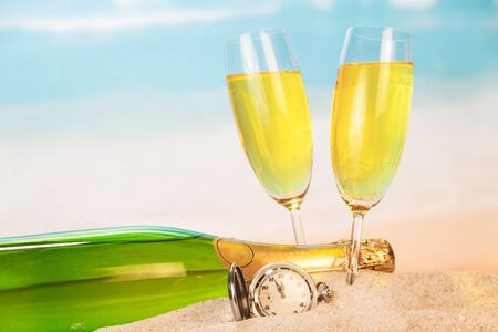 Bottle and two glasses with champagne, clock in the sand against the sea.の写真素材