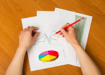 Female hands hold a pencil, graphs and sheet calculations on the desktop background.の写真素材
