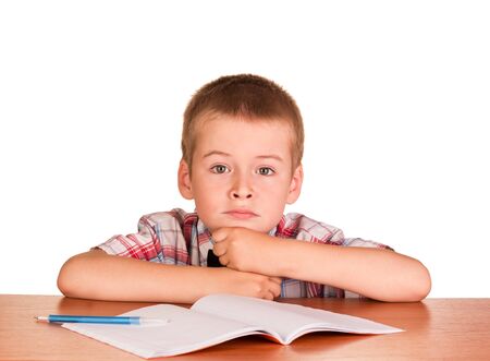 Sad boy sitting at a table on a notebook, a pen isolated on white background.の写真素材