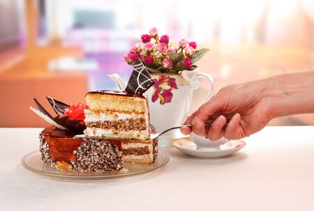 Hand holds a scapula with a piece of chocolate cream cake and cup of tea on a background of the kitchen.の写真素材