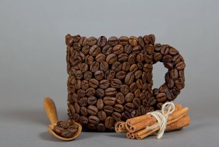 Cinnamon sticks, cup made of coffee beans, a spoon, on a gray background.の写真素材