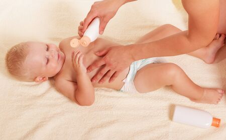 Mother's hands holding a bottle of milk for the little boy's body in a diaper lying on a towel. Background.の写真素材